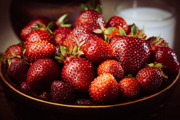 Red ripe strawberries in a brown clay plate with a glass of milk on the background