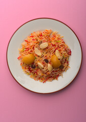 Colourful Pakistani Zarda rice on a white porcelain plate on pink background