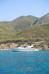 A luxury yacht anchored off the coast of Masua in southern Sardinia, Italy, with a mountainous landscape and unspoiled nature of the island in the background