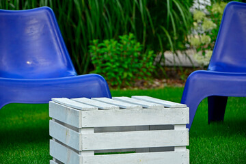 biały stolik ze skrzynki i niebieskie fotele ogrodowe na trawie, blue plastic garden chair on grass, garden table made of box, blue chairs and white wooden box in garden,  fotel ogrodowy "PS VAGO"