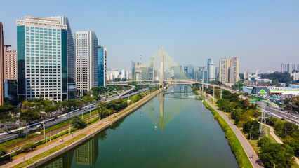 Vista do Rio Pinheiros com a Ponte Estaiada ao fundo, destacando a arquitetura moderna e o tr&aacute;fego em um cen&aacute;rio urbano de S&atilde;o Paulo