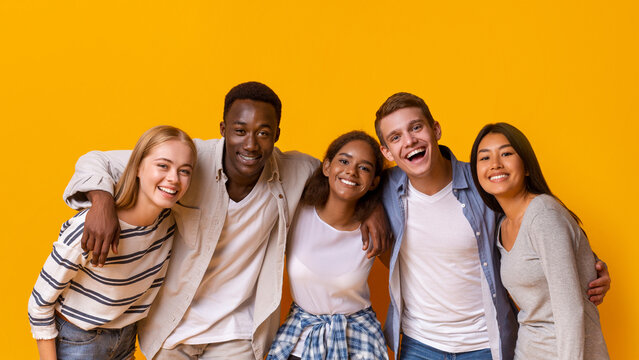 Friendly group of multiethnic students embracing and smiling over yellow background