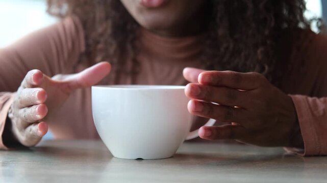 Women's hands hold a mug of hot tea in the morning during the cold season. A young woman warms her hands on a very hot cup of tea.