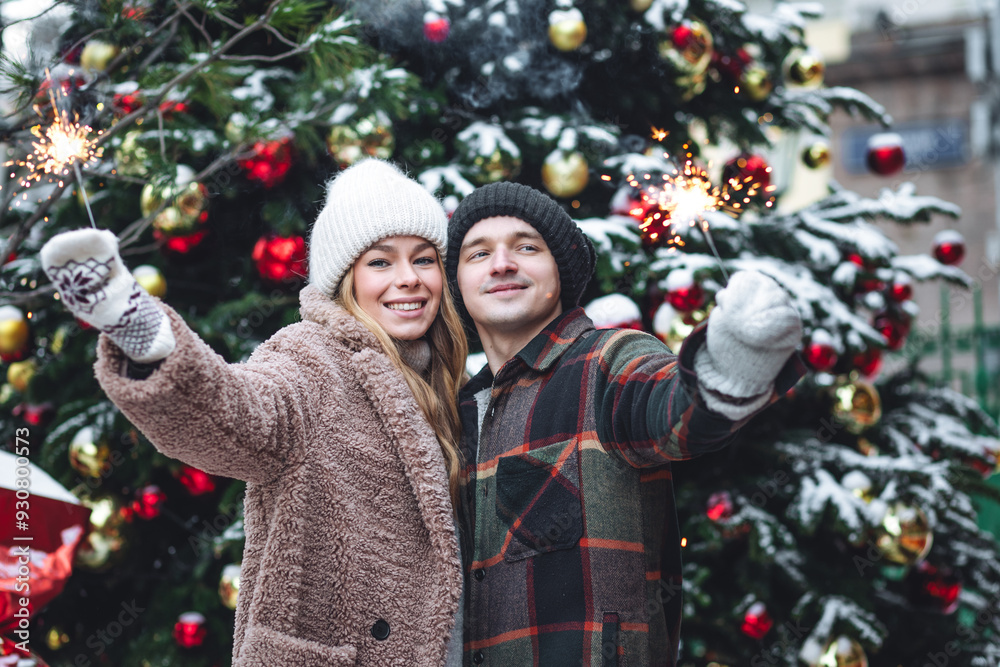 Wall mural beautiful young loving couple with sparklers in front of decorated christmas tree. celebrating new y