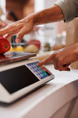 Close-up of male vendor utilizing digital scale to measure locally grown fruits and vegetables. Detailed image of weighing machine being used in a sustainable eco friendly grocery store.