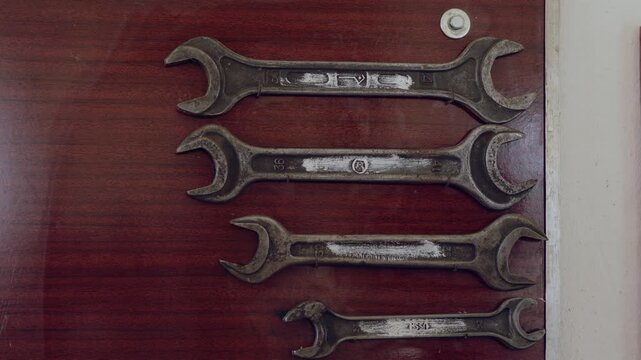 A hand is adjusting wrenches on a wooden door using mechanics tools in a garage