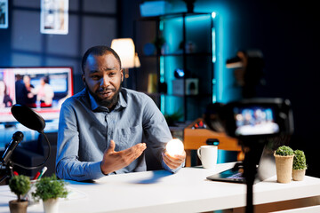 BIPOC influencer recording review of dimmable light bulb able to change into different colors. Tech guru presenting smart home automation technology controlled by voice commands