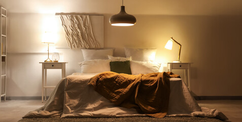 Interior of bedroom with plaid on bed and glowing lamps at night
