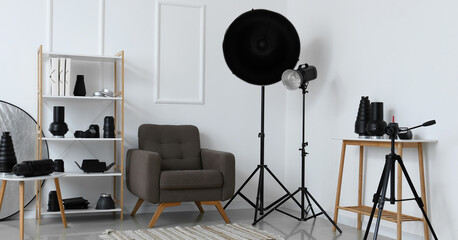 Interior of light photo studio with armchair, shelf unit and different modern equipment