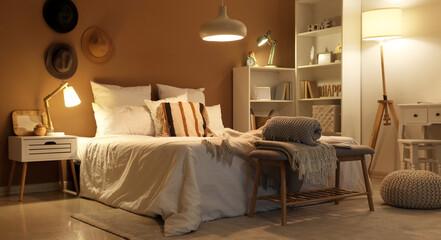 Interior of bedroom with plaids on soft bench and glowing lamps at night