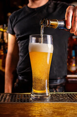 A bartender pours a bottled beer into a pilsner glass. 