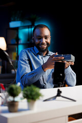 African american internet show host using smartphone on phone holder, filming content about V mount battery. Media star recording rechargeable accumulator review for video production fans