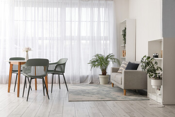 Interior of modern living room with table, chairs, sofa, houseplants and shelving unit