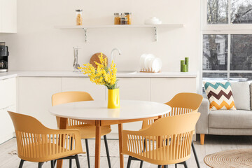 Interior of light modern interior of kitchen studio with dining table, mimosa flowers, armchairs, counters and sofa
