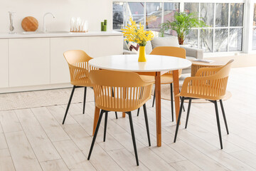 Interior of modern stylish kitchen studio with dining table, armchairs, mimosa flowers, houseplant, counters and sofa