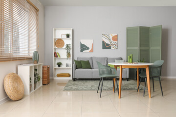 Stylish light living room with grey sofa, table and chairs