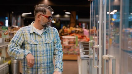 Handsome senior citizen man takes quail eggs from refrigerator in a food store