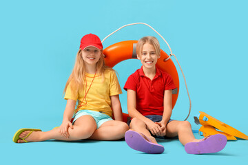 Happy little children lifeguards with ring buoy and flippers sitting on blue background © Pixel-Shot