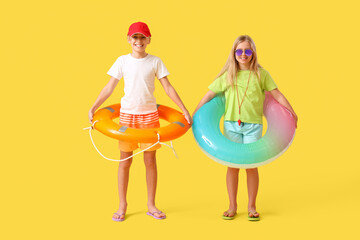 Happy little children lifeguards with lifebuoy and inflatable ring on yellow background