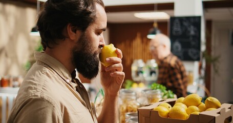 Man in zero waste store shops for farm grown fruits, getting dopamine rush while smelling them. Client experiences childhood nostalgic bliss while feeling nice lemons aroma in local shop, zoom in shot