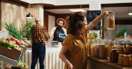 Zero waste supermarket customer roaming around aisles adding healthy natural pantry staples to shopping basket. Local neighborhood shop client shopping for additives free bulk food items
