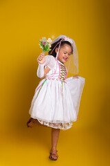 Cheerful child dressed as a bride holding a bouquet of flowers and posing for the camera.