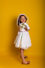 Cheerful child dressed as a bride holding a bouquet of flowers and posing for the camera.