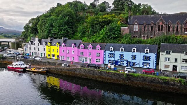Aerial view of Portree town with colourful houses and fishing boats in Scotland. Scenic view of the natural harbour and port by high ground and cliffs. Popular tourist destination on the Isle of Skye.