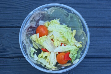 food from fresh green salad and red tomatoes in a plastic plate stands on a black wooden table
