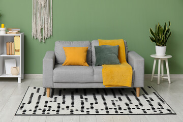Interior of living room with comfortable sofa, cushions, houseplants and yellow plaid