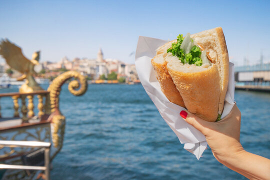 Tourist hand with balik ekmek fish sandwich with stunning views of the Bosphorus and Istanbul city skyline.