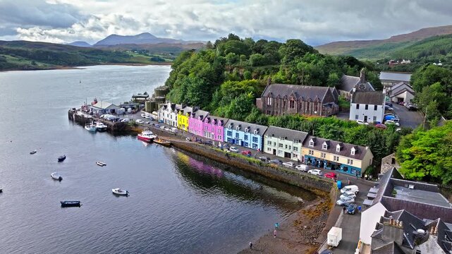 Aerial view of Portree town with colourful houses and fishing boats in Scotland. Scenic view of the natural harbour and port by high ground and cliffs. Popular tourist destination on the Isle of Skye.