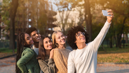 Happy teen international friends taking selfie while walking in autumn park, happy memories concept