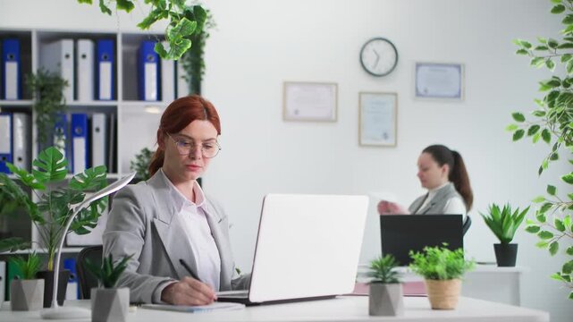 end of working day, young female office worker does not have time to finish work and argues with carefree colleague sitting in room