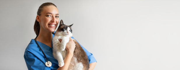 Portrait Of Happy Veterinarian Doctor Woman Holding A Cat, Posing With Healthy Feline Patient Over Gray Studio Background, Smiling At Camera. Pet Health Care And Routine Check Up Concept, Copy Space