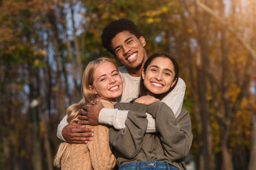 African guy hugging his pretty international girlfriends, walking by park and posing