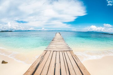 Obraz premium Wooden pier extending into turquoise ocean with white sand beach and clear water in a wide-angle view.