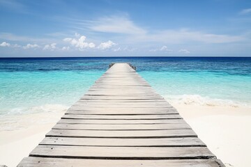 Wooden pier extending into turquoise ocean with white sand beach and clear water in a wide-angle view.