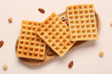 Wooden board with tasty Belgian waffles and nuts on beige background