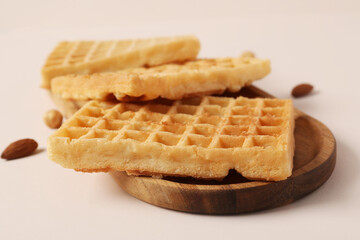Wooden board with tasty Belgian waffles and nuts on beige background