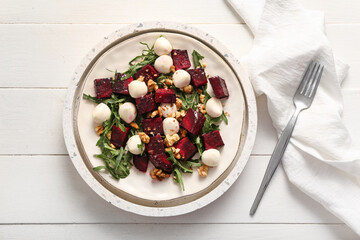 Plate of fresh salad with beet and mozzarella cheese on white wooden background