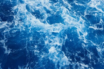 Fototapeta premium Top view of blue ocean water with intricate wave textures and water splashes, creating an abstract background of the sea surface, showcasing the dynamic movement and vibrant blue tones of the ocean.