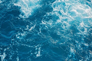Obraz premium Top view of blue ocean water with intricate wave textures and water splashes, creating an abstract background of the sea surface, showcasing the dynamic movement and vibrant blue tones of the ocean.