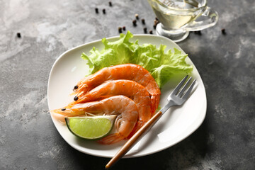 Plate with tasty boiled shrimps, lettuce and lime on dark background