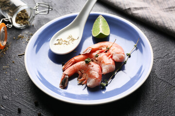 Plate with tasty boiled shrimps, lime and spoon of sauce on dark background