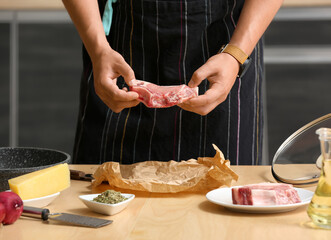 Young man cooking meat at table in kitchen, closeup