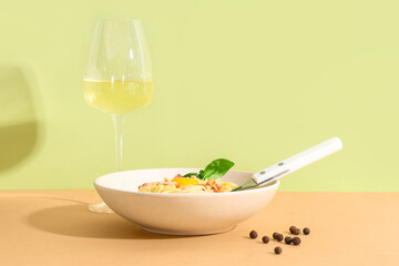 Bowl with tasty pasta carbonara and glass of wine on beige table