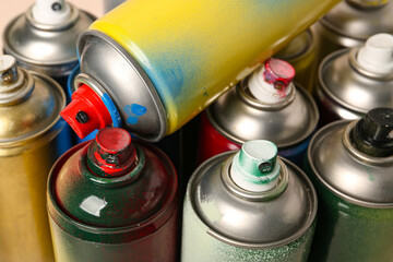 Many spray paint cans on beige background, closeup