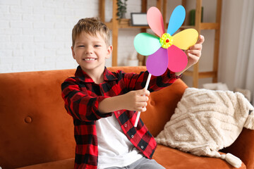 Cute little boy with toy windmill sitting on sofa at home