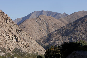 A rugged, rocky mountain landscape under a clear blue sky, showcasing the natural beauty of the region with contrast between rocky cliffs and green vegetation.